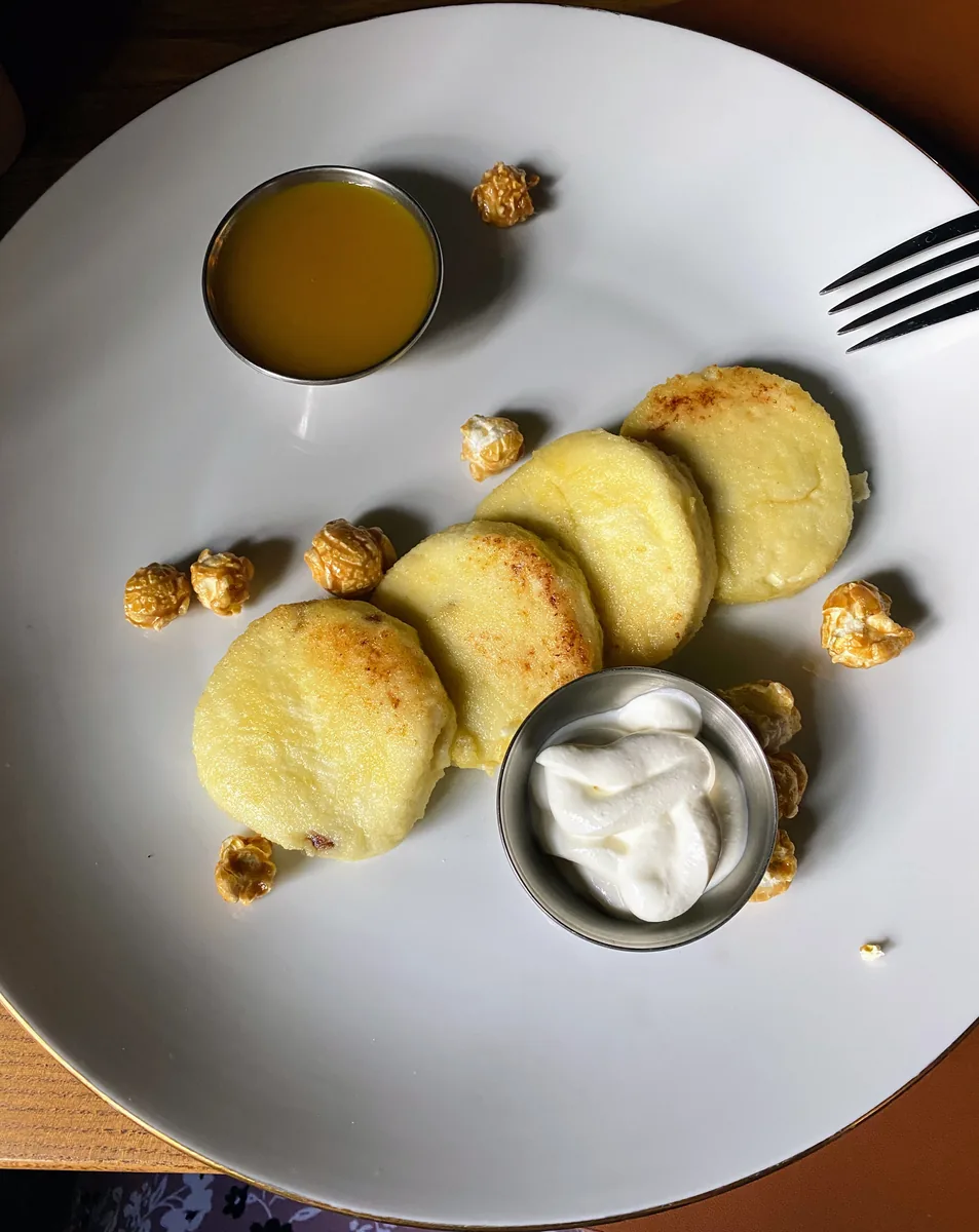 Сырники на белой тарелке со сметаной и соусом